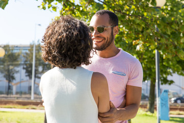 Wall Mural - Cheerful multiethnic friends holding hands in park. Happy multiracial man and woman greeting each other in park. Friendship concept