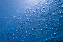 Water Drops On Waterproof Nylon Fabric. Macro Detail View Of Texture Of Blue Woven Synthetic Waterproof Clothing. Morning Dew On Camping Tent Close View. Rain