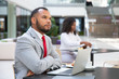 © Mangostar - Pensive businessman with laptop thinking over startup strategy over cup of coffee. Young African American woman drinking coffee in background. Working in cafe concept