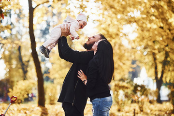 Wall Mural - Cheerful family having fun together with their child in beautiful autumn park