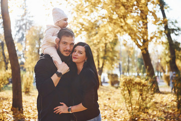 Wall Mural - Cheerful family having fun together with their child in beautiful autumn park