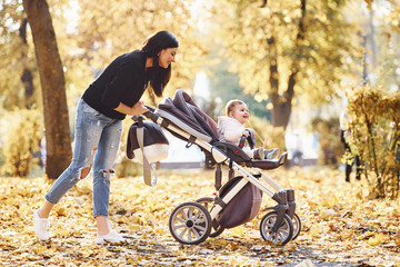 Wall Mural - Mother in casual clothes with her child in pram is in the beautiful autumn park