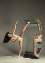 Wall Mural - Young and stylish modern ballet dancer on brown background with mirror. Illusion reflections on surface. Magic of flexibility, motion. Parallel dreamworld. Concept of creative art, action, inspiring.