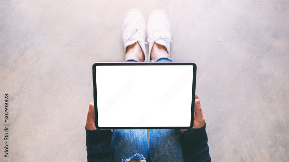 Top view mockup image of a woman holding black tablet pc with blank white screen while sitting on the floor - obrazy, fototapety, plakaty 