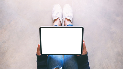 Top view mockup image of a woman holding black tablet pc with blank white screen while sitting on the floor