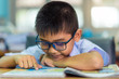 © pop_thailand - Asian elementary school boy in a white school uniform and wearing glasses, is reading a book in the classroom.
