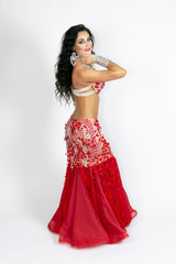 Girl in a red dress for oriental dancing. Brunette in beautiful long red dress to perform belly dance on a white background.