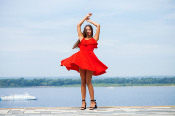 Wall Mural - Young beautiful girl in red dress walking on the summer street