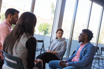 Creative professional group discussing startup project. Young business men and women in casual sitting in training room opposite of each other and talking. Corporate meeting concept