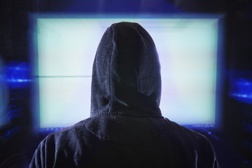Wall Mural - anonymous hacker is looking at computer monitor. view from behind.