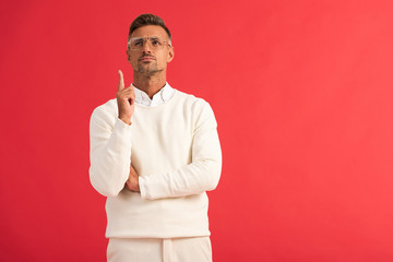 handsome man in glasses looking up while pointing with finger isolated on red