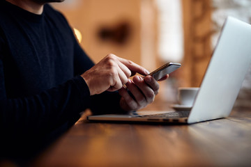 man using his mobile phone above laptop keyboard
