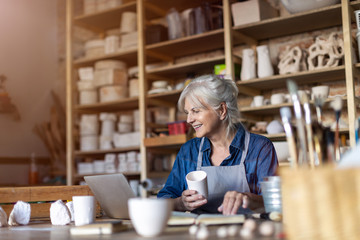 Wall Mural - Mature woman pottery artist using laptop in art studio 