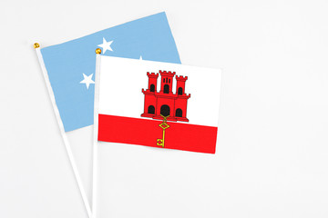 Gibraltar and Micronesia stick flags on white background. High quality fabric, miniature national flag. Peaceful global concept.White floor for copy space.