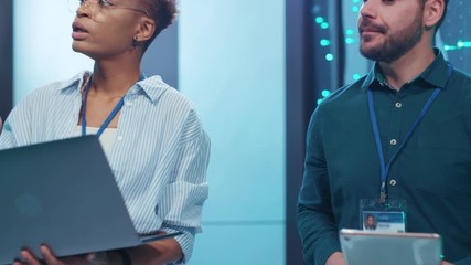 Wall Mural - male and female it technicians walking in digital corridor of server cluster doing backup operations