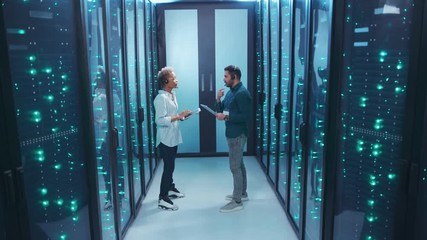 Wall Mural - couple of mixed-race technicians walking in database corridor of server room discussing work solving