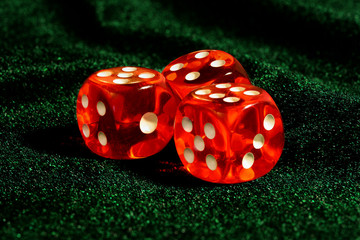 Three red acrylic transparent dices for games. Gambling translucent dices on dark-green velvet surface, close-up, large depth of field.