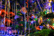 Silver tinsel on Christmas tree. Blurred holiday background with garland, glass toys, balls, lights. Colorful decoration close-up.