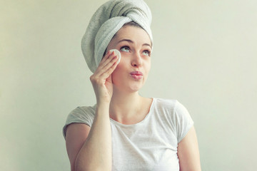 Wall Mural - Beauty portrait of smiling woman in towel on head with soft healthy skin removing make up with cotton pad isolated on white background. Skincare cleansing spa relax concept