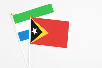 East Timor and Sierra Leone stick flags on white background. High quality fabric, miniature national flag. Peaceful global concept.White floor for copy space.