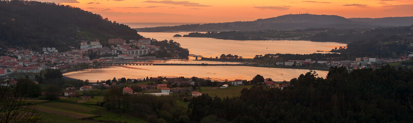 Wall Mural - Serene dusk panorama of the medieval fishing town of Pontedeume with its iron and stone bridge orange sky La Coruña Galicia