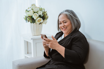 Wall Mural - Old woman confident is seriously beautiful when using smartphone sitting on the sofa