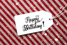 Label With English Calligraphy Happy Birthday. Red Wrapping Paper As Background With Snowflakes