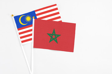 Wall Mural - Morocco and Malaysia stick flags on white background. High quality fabric, miniature national flag. Peaceful global concept.White floor for copy space.