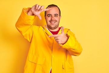 Sticker - Young man wearing rain coat standing over isolated yellow background smiling making frame with hands and fingers with happy face. Creativity and photography concept.