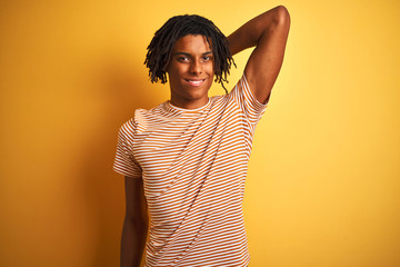 Wall Mural - Afro man with dreadlocks wearing striped t-shirt standing over isolated yellow background smiling confident touching hair with hand up gesture, posing attractive and fashionable