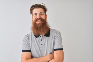 Young redhead irish man wearing grey polo standing over isolated white background happy face smiling with crossed arms looking at the camera. Positive person.