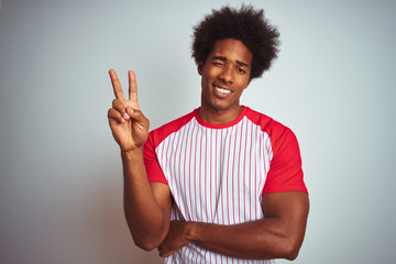 Sticker - African american man with afro hair wearing red striped t-shirt over isolated white background smiling with happy face winking at the camera doing victory sign. Number two.