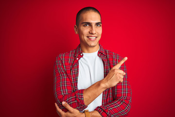 Poster - Young handsome man wearing a shirt using watch over red isolated background with a big smile on face, pointing with hand and finger to the side looking at the camera.