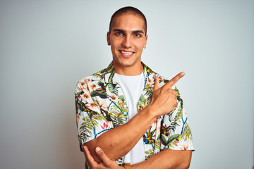 Poster - Young handsome man on holidays wearing Hawaiian shirt over white background with a big smile on face, pointing with hand and finger to the side looking at the camera.