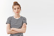 Self-assured confident young skeptical woman with messy bun in striped t-shirt, cross hands chest and smirk feeling superiour and encouraged, stare unconvinced over white background