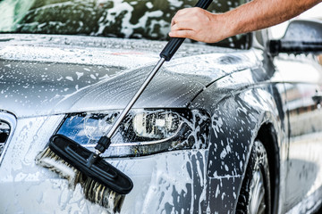 Washing front light on luxury car with brush and foam. Cleaning vehicle concept close up.