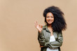 Leinwandbild Motiv Indoor shot of pleasant looking curly woman has pleasant smile, makes okay gesture, excellent sign, gives approval, dressed in fashionable leather shirt, isolated over brown wall, blank space on left