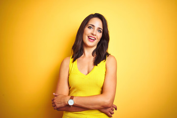 Wall Mural - Young beautiful woman wearing t-shirt standing over yellow isolated background happy face smiling with crossed arms looking at the camera. Positive person.