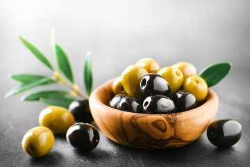 Wall Mural - Fresh olives with core in olive bowl on dark stone table and green leaves.