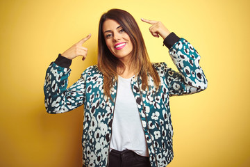 Canvas Print - Young beautiful woman wearing casual jacket over yellow isolated background smiling pointing to head with both hands finger, great idea or thought, good memory