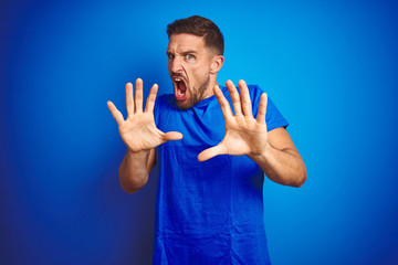 Sticker - Young handsome man wearing casual t-shirt over blue isolated background afraid and terrified with fear expression stop gesture with hands, shouting in shock. Panic concept.