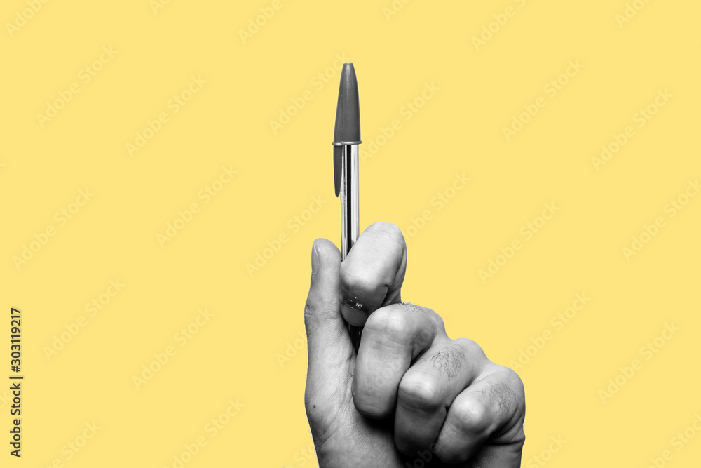 Concept of freedom of speech and information, stop censorship. Hand holding a pen in sign of protest, the pressure of censorship. Yellow background. Black and white image - obrazy, fototapety, plakaty 