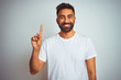 © Krakenimages.com - Young indian man wearing t-shirt standing over isolated white background showing and pointing up with finger number one while smiling confident and happy.