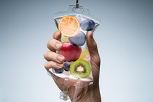 Human Hand Holding Saline Bag With Fruit Slices Over Grey Background