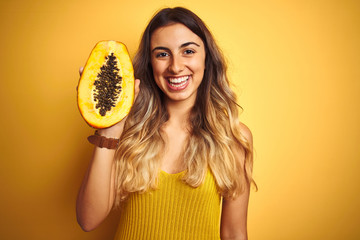 Sticker - Young beautiful woman holding papaya over yellow isolated background with a happy face standing and smiling with a confident smile showing teeth