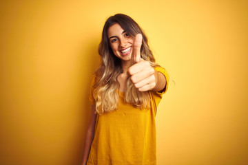 Sticker - Young beautiful woman wearing t-shirt over yellow isolated background doing happy thumbs up gesture with hand. Approving expression looking at the camera with showing success.