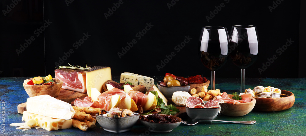 Italian antipasti wine snacks set. Cheese variety, Mediterranean olives, seafood salad, Prosciutto di Parma, tomatoes, anchovy and wine in glasses - obrazy, fototapety, plakaty 