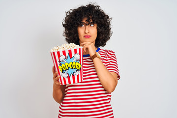 Wall Mural - Young arab woman with curly hair holding pack of popcorns over isolated white background serious face thinking about question, very confused idea