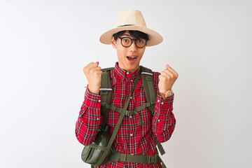 Sticker - Chinese hiker man wearing backpack canteen glasses hat over isolated white background celebrating surprised and amazed for success with arms raised and open eyes. Winner concept.