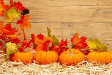 Fall Scene With Orange Pumpkins And Fall Leaves On Straw Hay With Weathered Wood Background